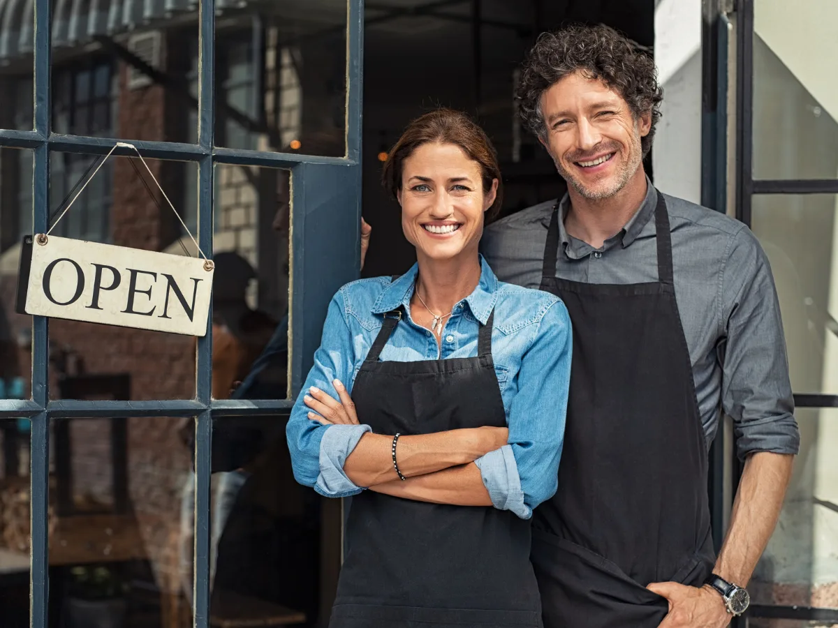 Small business owners standing in the doorway of their open shop